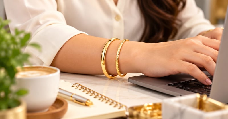Daily wear gold bangles design: a plain 22K churi and a slim textured bangle on a woman's wrist at an office desk